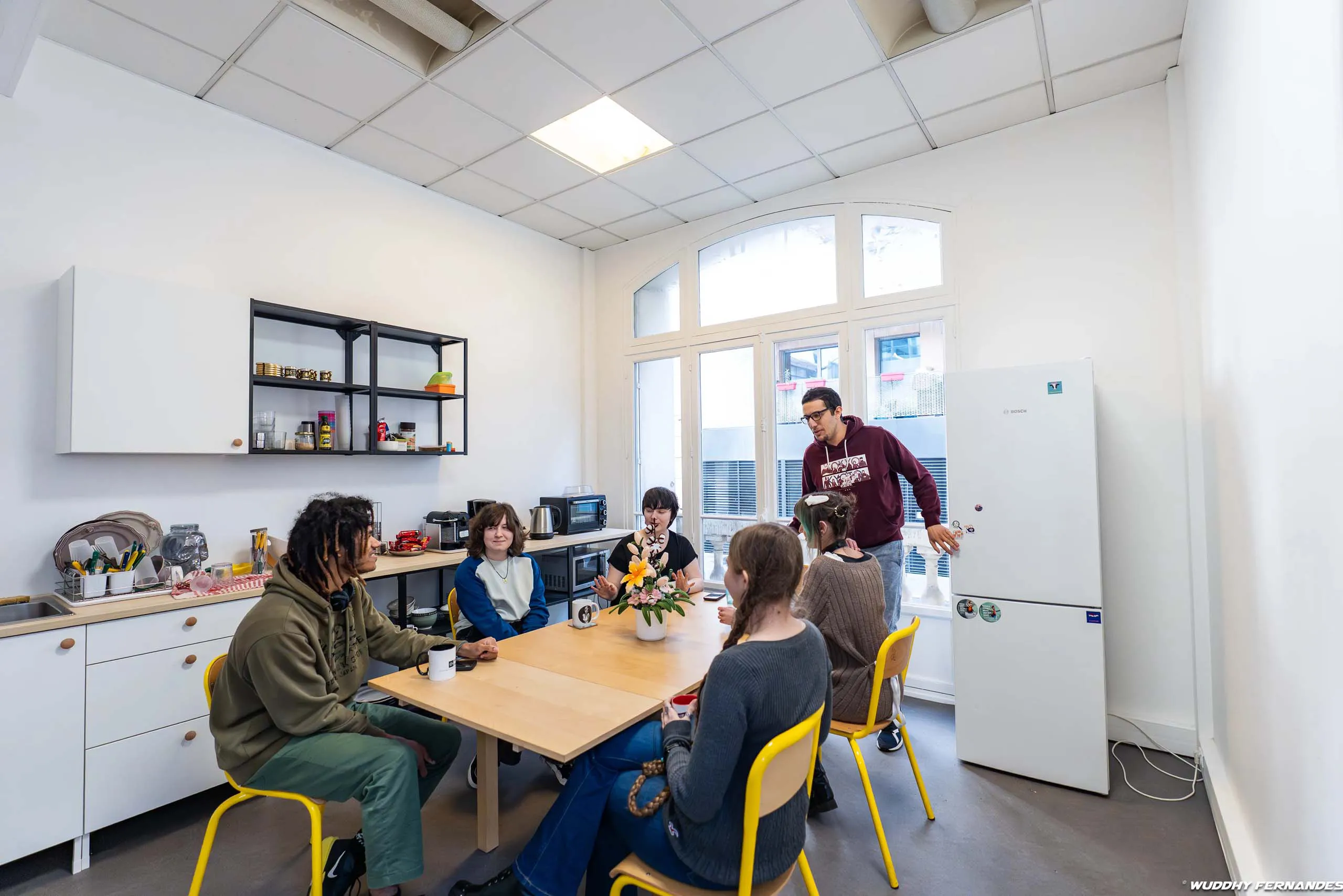 Trois personnes travaillent sur des ordinateurs dans un espace de travail collaboratif, avec un formateur qui accompagne une participante devant un ordinateur.
