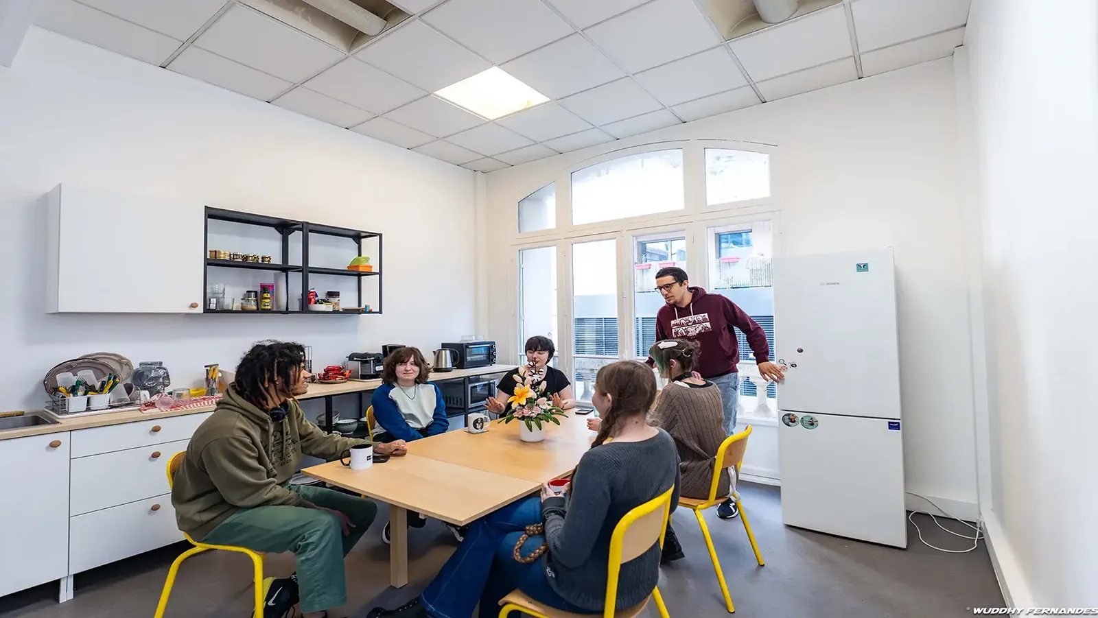 Groupe d’étudiants et formateur discutant autour d’une table dans un espace cuisine et détente d’un centre de formation.