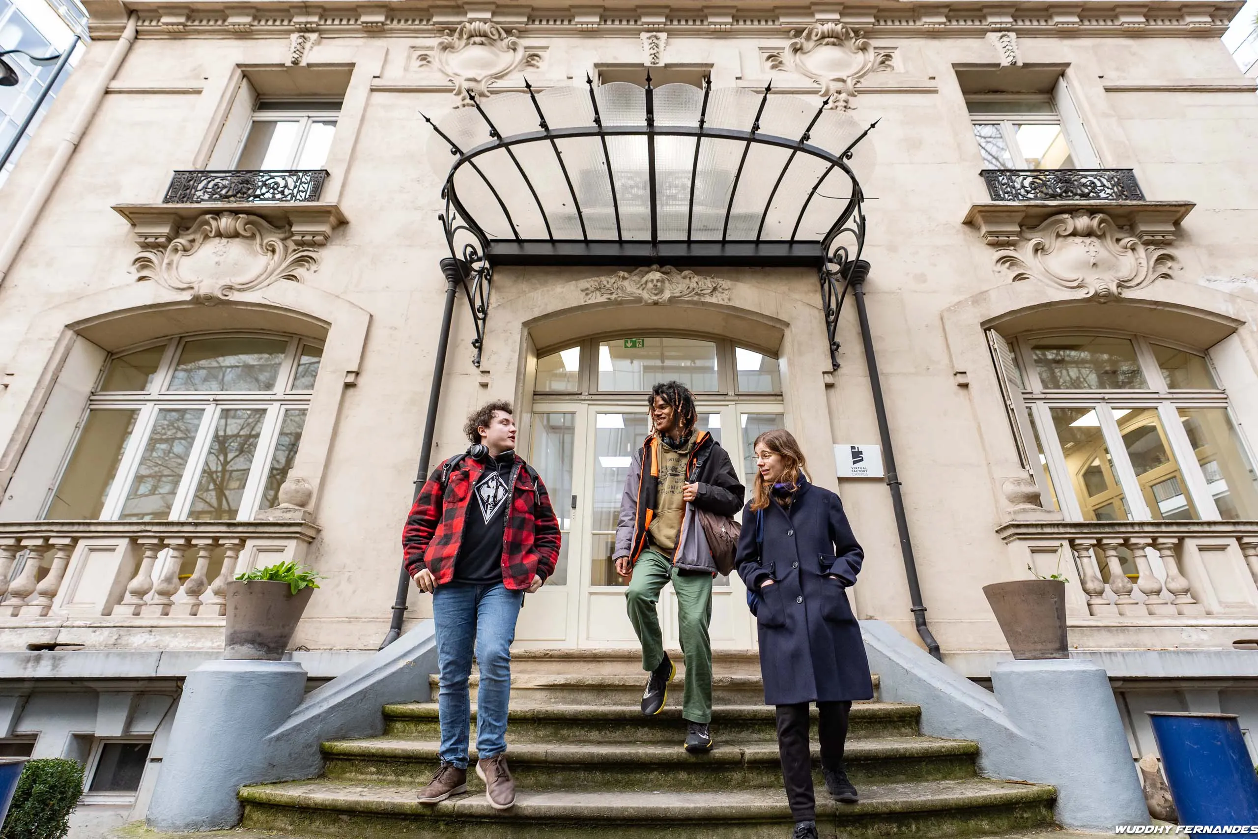 Étudiants sortant du campus Virtual Factory devant un bâtiment historique.