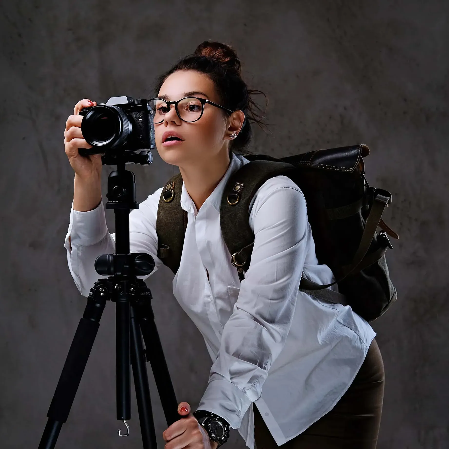 Photographe en train de régler un appareil photo sur trépied pour une prise de vue en studio.